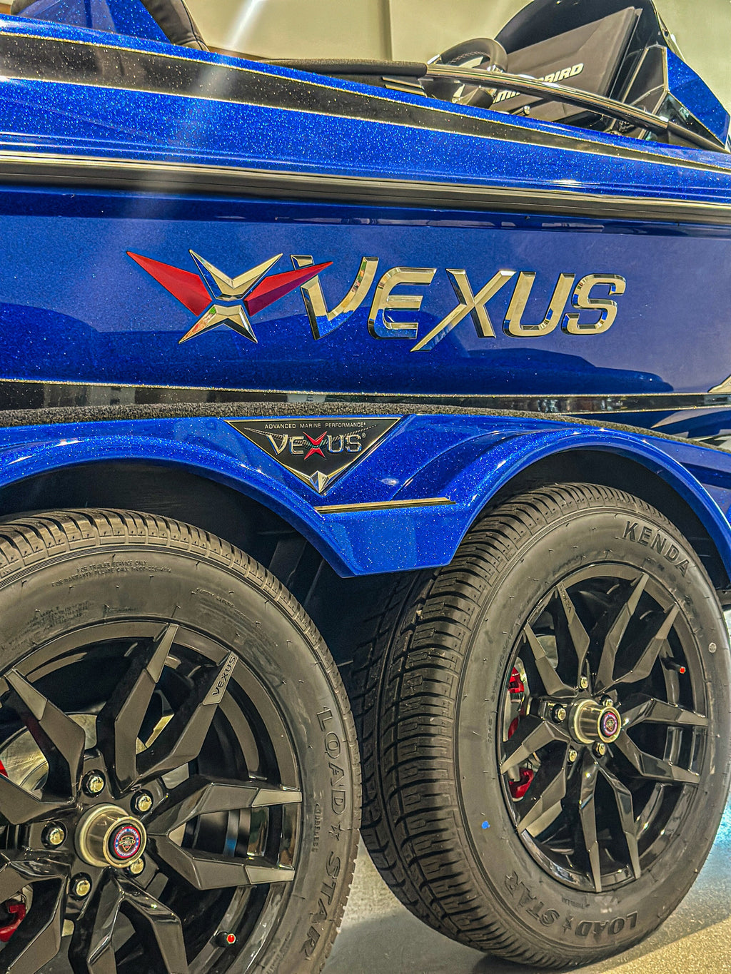Blue metal flake hull side and VEXUS badge above the tandem-axle Vexus trailer — 2025 Vexus VXS20, Lake & Trail USA, Okeechobee FL