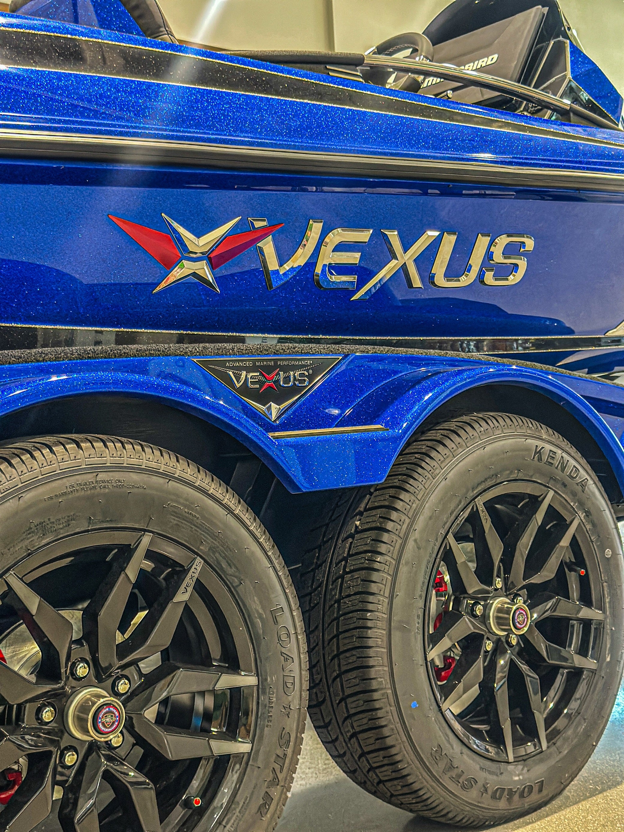 Blue metal flake hull side and VEXUS badge above the tandem-axle Vexus trailer — 2025 Vexus VXS20, Lake & Trail USA, Okeechobee FL